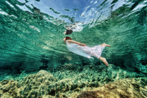 Swimming in transparent sea, emerges from clear sea, wearing fashionable white dress, luxury summer vacation, freedom and enjoyment concept